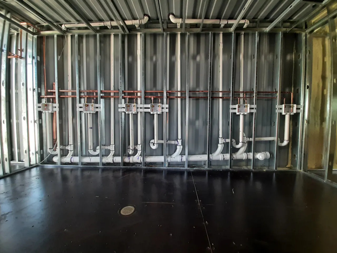 Organized water and drain piping inside open commercial wall framing